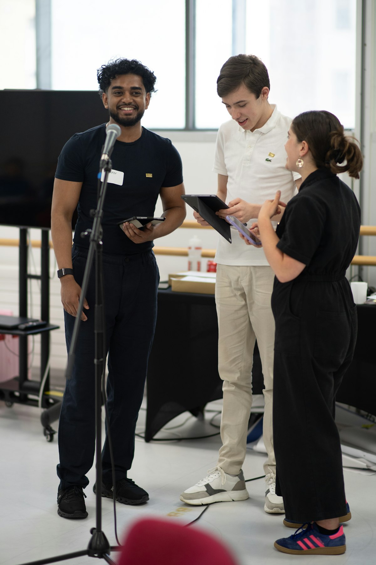 Two young facilitators holding iPads, stand at the front of the room smiling and preparing to present